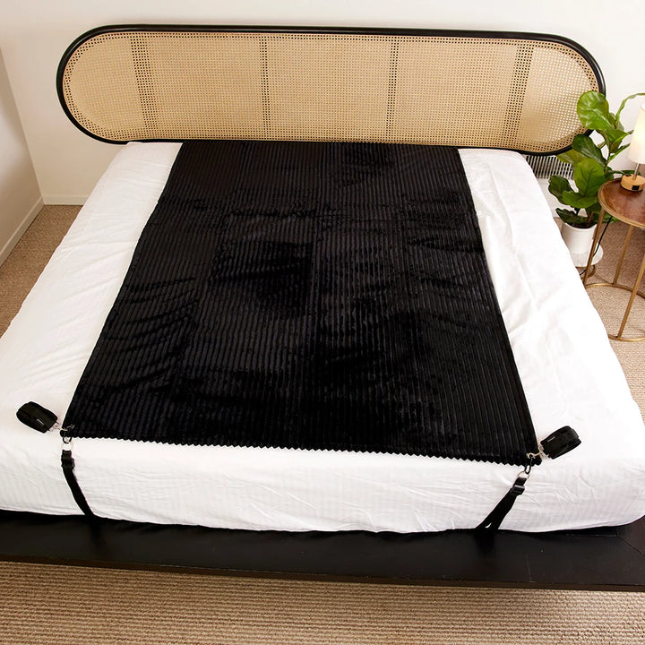 Black ribbed waterproof blanket spread across a bed, anchored at the corners
